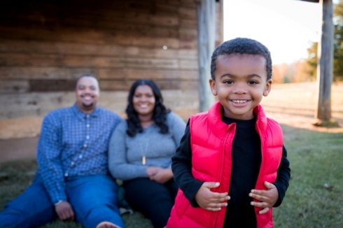 At Joyner Park in Wake Forest, NC, a child in a red vest smiles with his parents in the background.