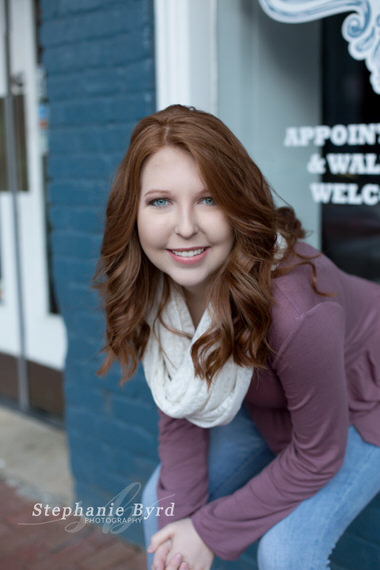 A girl with long red hair poses for senior portraits in downtown Raleigh, NC.