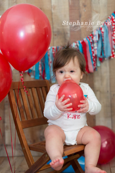 A small child holds a red balloon while sitting in a photographer's indoor studio.