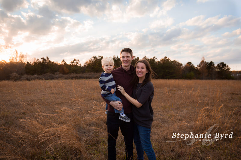 A family of three poses in a field at sunset for their family photos in McGees Crossroads.